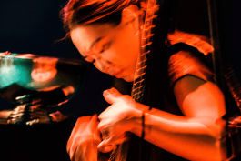 Lucy Zhao performing the pipa in a contemporary concert setting with red stage lighting 